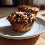 A close-up of a freshly baked Banana Chocolate Chip Muffin with a crumbly top, resting on a small white plate.