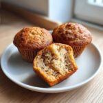 Close-up of three Cottage Cheese Banana Muffins, one cut open showing the moist, fluffy interior texture.