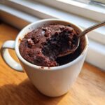 A spoonful of rich, dark Microwave Brownie in a Mug being lifted out, topped with chocolate chips.
