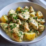 Close-up of One-Pan Creamy Garlic Herb Chicken and Potatoes coated in a rich sauce and sprinkled with fresh parsley.