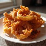 A close-up, featured image showing a mound of golden brown, crispy Onion Rings Extra Crispy piled high on a white plate.