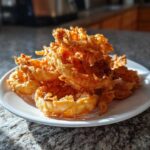 A tall pile of golden brown, super crispy Onion Rings Extra Crispy stacked high on a white plate.