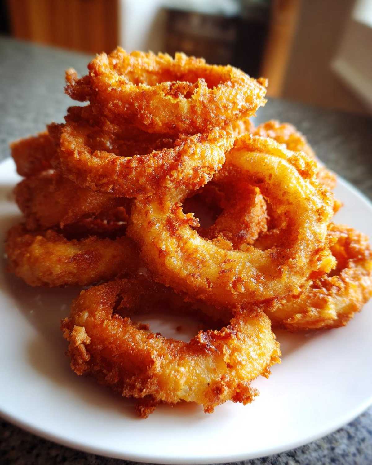 A tall stack of golden brown Onion Rings Extra Crispy piled high on a white plate.