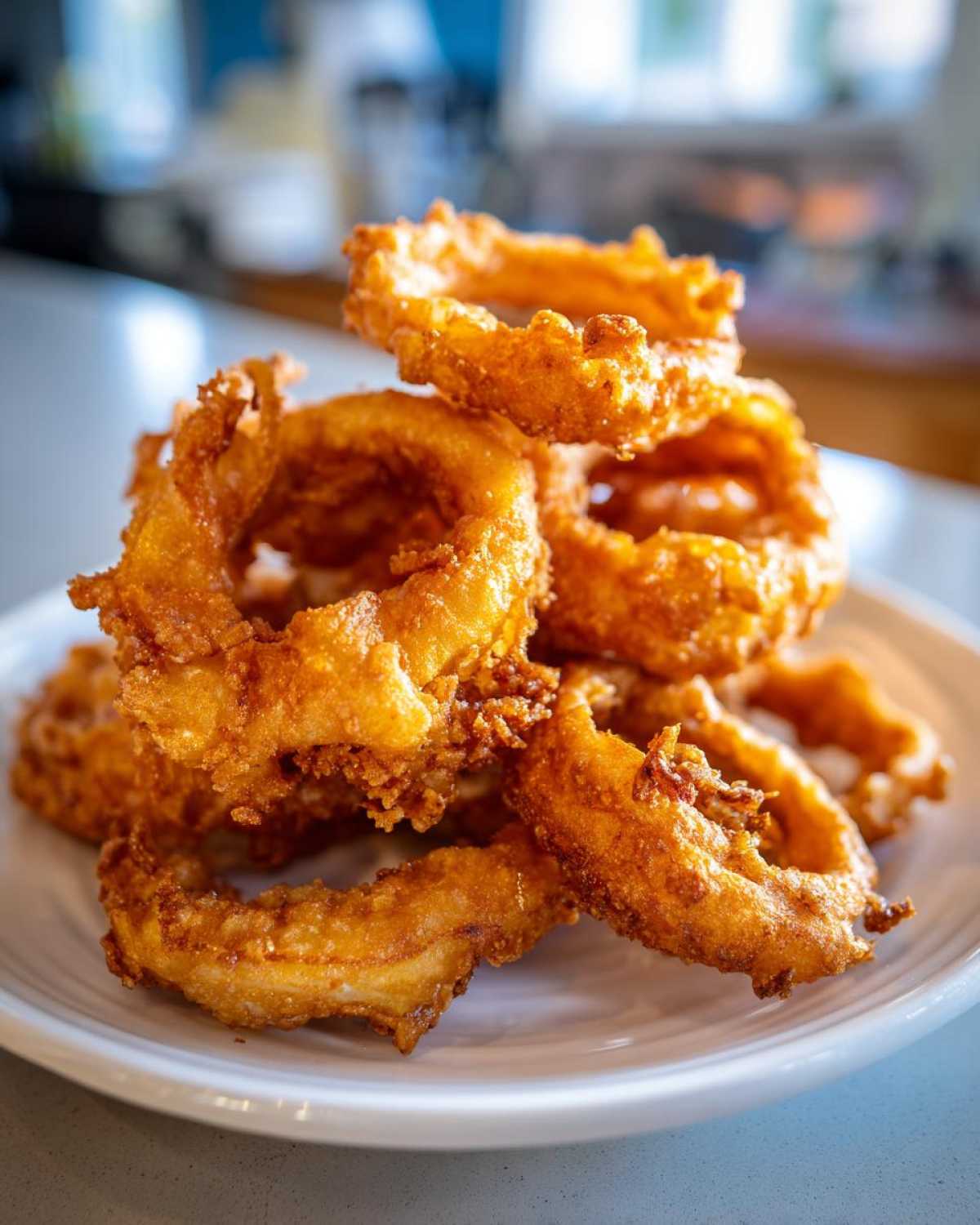 A tall stack of golden brown Onion Rings Extra Crispy piled high on a white plate.