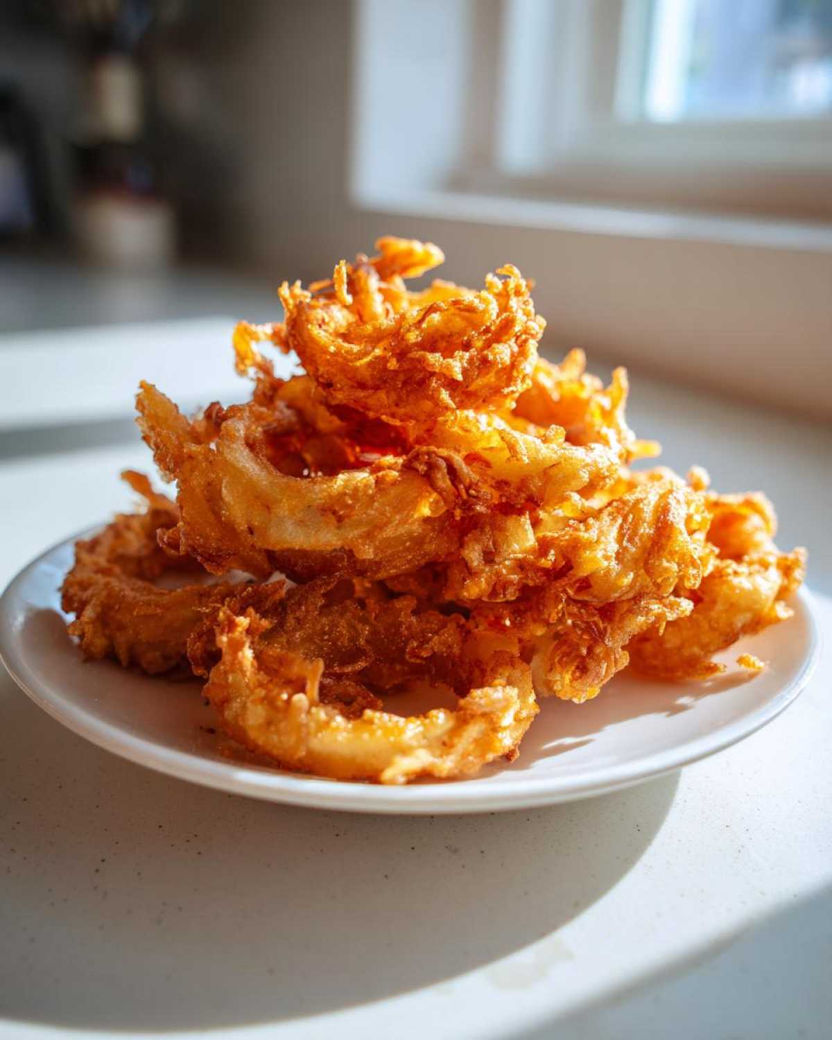 A tall stack of golden brown, heavily battered Onion Rings Extra Crispy piled high on a small white plate.