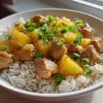 A close-up of Pineapple Chicken and Rice served over white rice, garnished with chopped green onions.