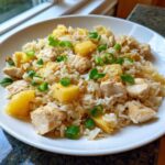 A close-up serving of Pineapple Chicken and Rice, featuring white rice, diced chicken, and chunks of pineapple, garnished with green onions.