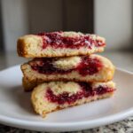 Close-up of three stacked slices of perfect raspberry swirl shortbread cookies showing the buttery base and bright red jam filling.