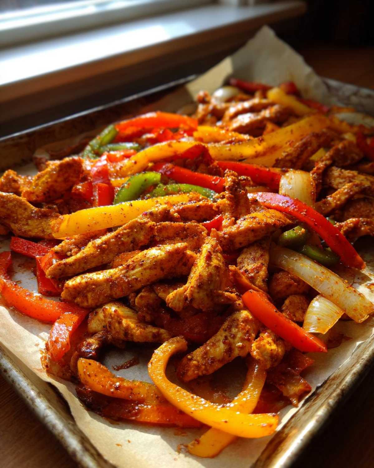 Close-up of seasoned chicken strips and colorful bell peppers for Sheet Pan Chicken Fajitas on a baking sheet.