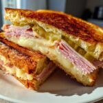 Close-up of a halved Sizzling Cuban Grilled Cheese sandwich showing melted cheese, ham, and pickles on toasted bread.