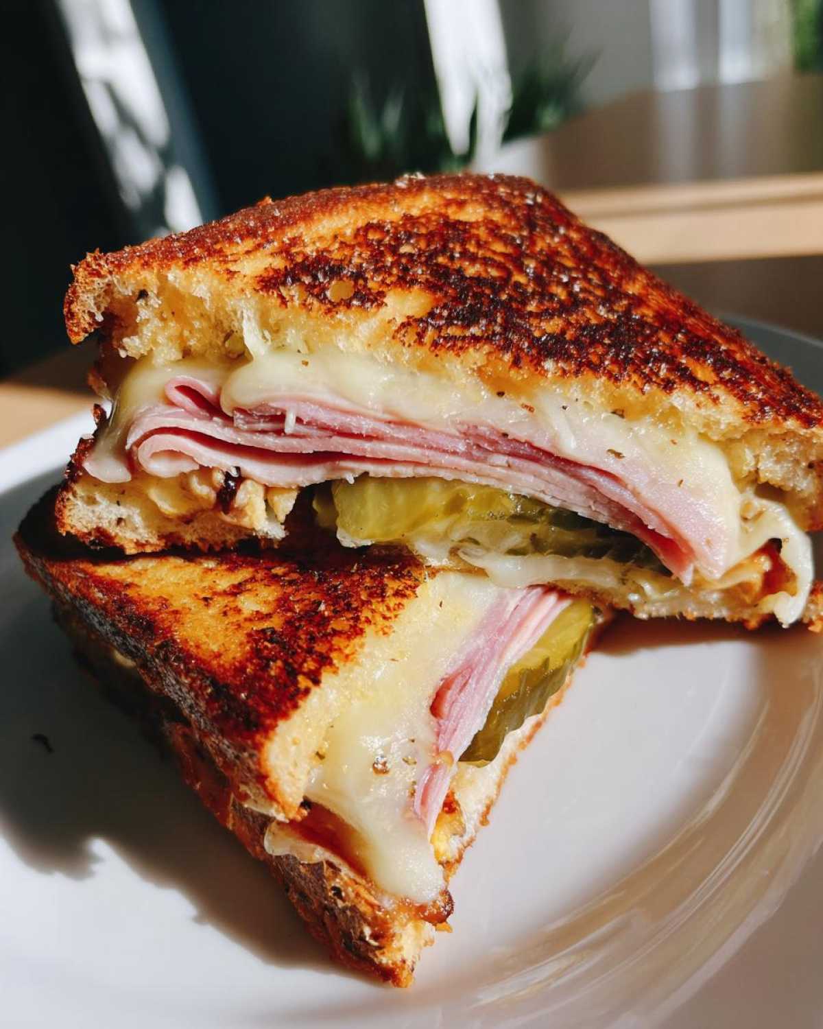 Close-up of a Sizzling Cuban Grilled Cheese sandwich cut in half, showing melted cheese, ham, and pickle slices.