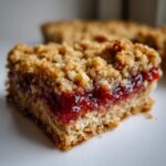 A close-up of a single square of Sourdough Breakfast Oatmeal Jam Bars showing the thick jam layer and crumbly topping.