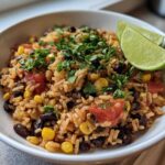A close-up of Southwest Beans and Rice One Pot dish topped with cilantro and served with lime wedges.