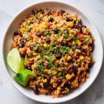 A white bowl filled with flavorful Southwest Beans and Rice, garnished with cilantro and lime wedges.