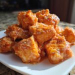 Close-up of a pile of Spicy Oven Baked Bang Bang Salmon Bites coated in creamy orange sauce and sprinkled with sesame seeds.
