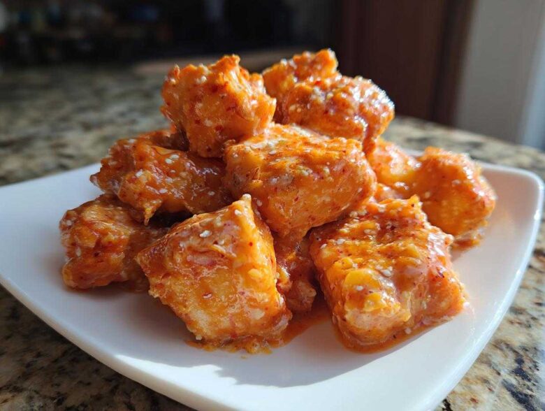 Close-up of a pile of Spicy Oven Baked Bang Bang Salmon Bites coated in creamy orange sauce and sprinkled with sesame seeds.