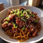 A close-up of Sticky Garlic Chicken Noodles topped with sesame seeds and green onions in a white bowl.