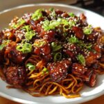 Close-up of Sticky Garlic Chicken Noodles coated in a dark glaze, topped with sesame seeds and green onions.