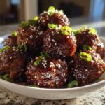 A close-up of glistening Sticky Hoisin Meatballs Appetizer piled in a white bowl, topped with sesame seeds and green onions.