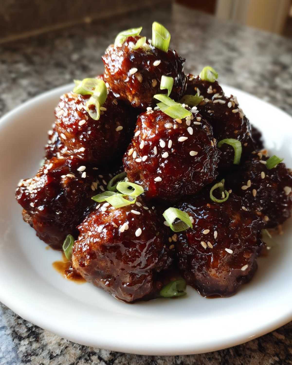 A close-up of Sticky Hoisin Meatballs Asian Appetizer piled high, coated in dark glaze and topped with sesame seeds and green onions.