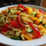 Close-up of a vibrant Veggie Rainbow Orzo Salad featuring orzo pasta, red and yellow peppers, and cucumber chunks.