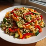 Close-up of a bright Veggie Rainbow Orzo Salad featuring orzo pasta, red and orange peppers, and cucumber slices.