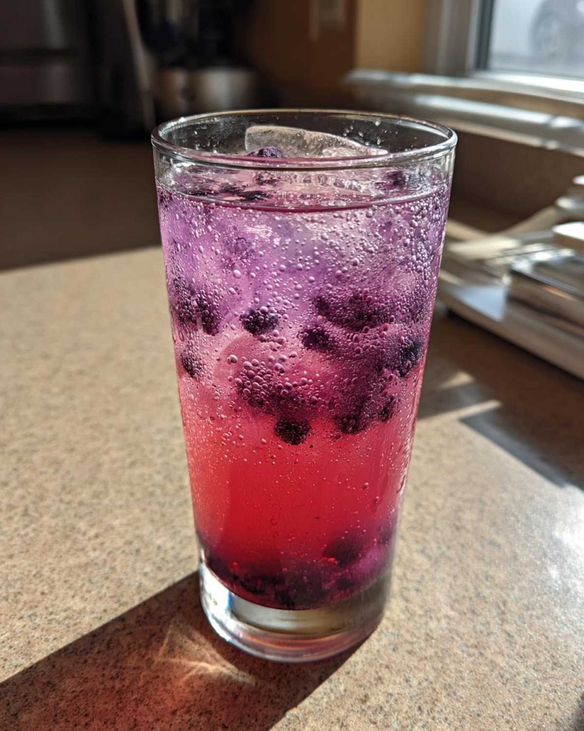 Close-up of a tall glass filled with vibrant, layered Blueberry Lemonade, ice, and whole blueberries.