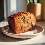 A thick slice of moist Apple Cinnamon Bread sitting on a small ceramic plate, highlighted by warm sunlight.