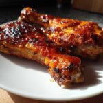 Two glossy, caramelized Baked Chicken Legs resting on a white plate, highlighted by strong sunlight.