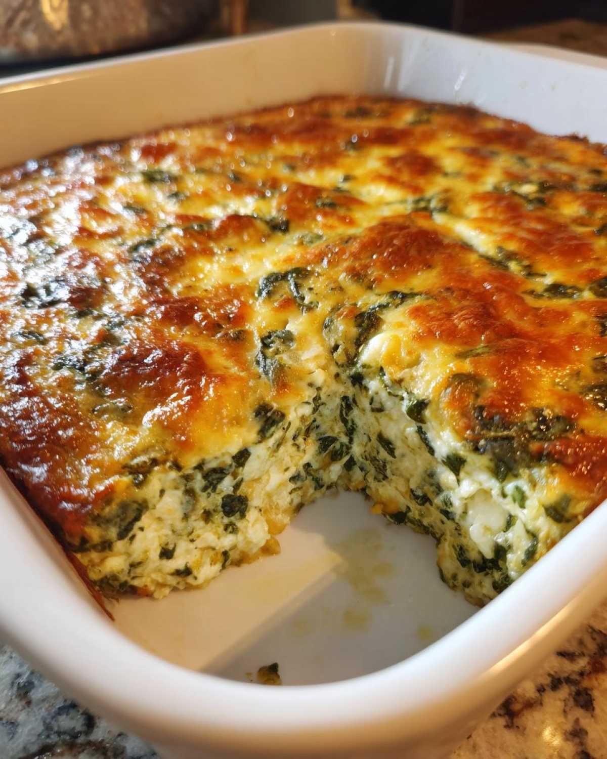 A square white baking dish filled with hot, creamy Spinach Dip, showing a portion removed to reveal the cheesy, baked interior.