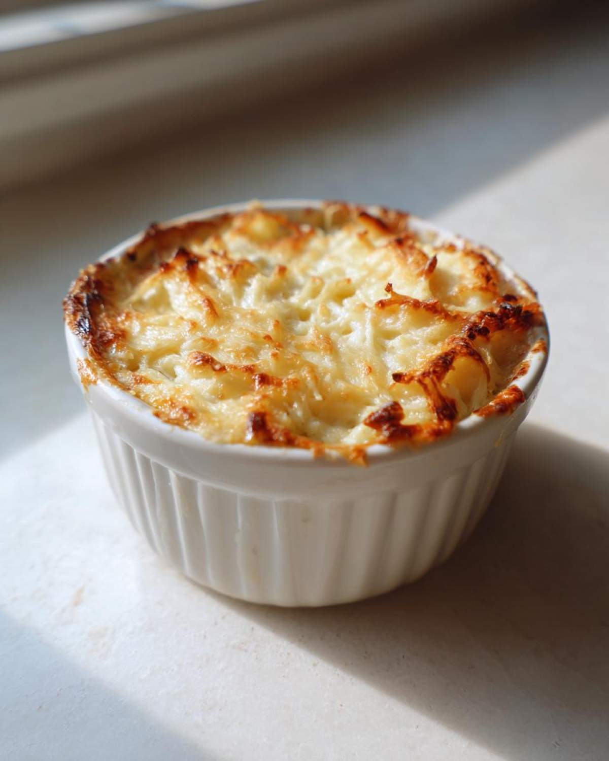 A small, individual serving of hot Baked Pickle Dip with a golden, bubbly, and slightly browned cheese topping.