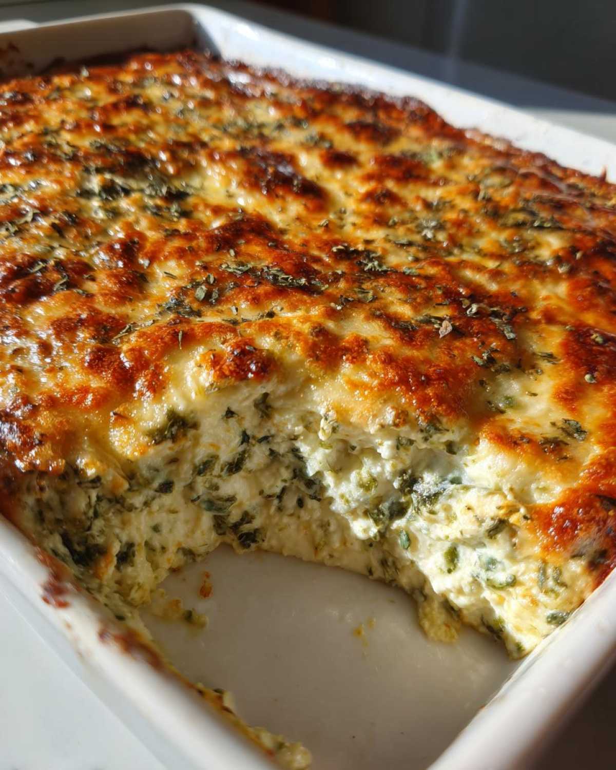 Close-up of a freshly baked, creamy Spinach Dip in a white casserole dish with a scoop removed.