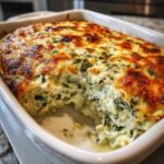 A close-up of hot, creamy Spinach Dip baked in a white dish with a golden-brown, bubbly cheese crust.