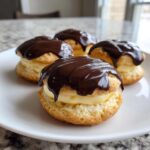Four delicious Boston Cream Pie Cookie Bites filled with cream and topped with dripping chocolate ganache on a white plate.