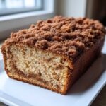 A freshly baked Cinnamon Crumb Banana Bread Loaf with a thick, sugary cinnamon topping, shown on a white platter.
