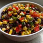 Close-up of vibrant Cowboy Caviar Dip featuring black beans, corn, diced tomatoes, and cilantro in a white bowl.