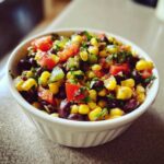 Close-up of a white bowl filled with fresh Cowboy Caviar Dip ingredients: corn, black beans, tomatoes, and cilantro.