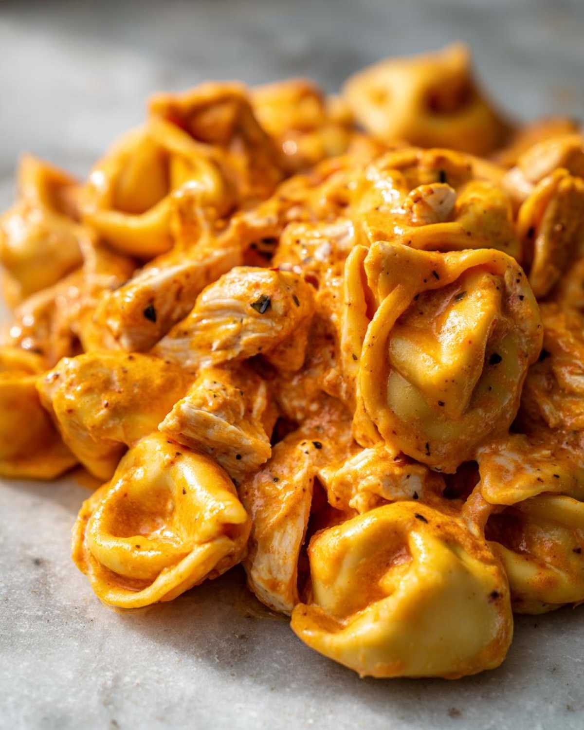 Close-up of tortellini pasta coated in a rich, creamy orange sauce with chunks of chicken, part of the Marry Me Chicken Tortellini recipe.