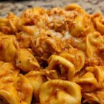 A close-up view of cheesy, creamy Marry Me Chicken Tortellini coated in a rich, orange-red sauce.