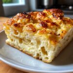 A thick, airy slice of Garlic Parmesan Focaccia Bread showing a cheesy, open crumb structure and golden-brown topping.