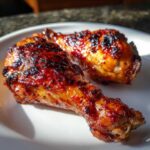 Two perfectly cooked, glazed Baked Chicken Legs with caramelized, slightly charred skin on a white plate.