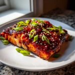 A perfectly cooked fillet of Gochujang Honey Glazed Salmon topped with sesame seeds and sliced green onions.