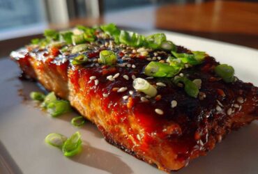 A close-up of a perfectly cooked Gochujang Honey Glazed Salmon fillet topped with sesame seeds and fresh green onions.