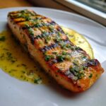 A perfectly cooked fillet of Grilled Salmon with Lemon Butter Sauce, showing char marks and fresh herbs.