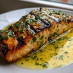 Close-up of a perfectly cooked piece of Grilled Salmon with Lemon Butter Sauce, glistening with herbs.