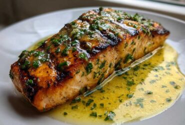 Close-up of a perfectly cooked piece of Grilled Salmon with Lemon Butter Sauce, glistening with herbs.