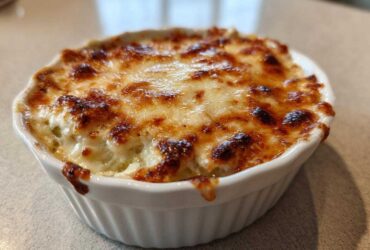 A close-up of hot Baked Pickle Dip bubbling in a white ramekin with a perfectly browned and melted cheese topping.