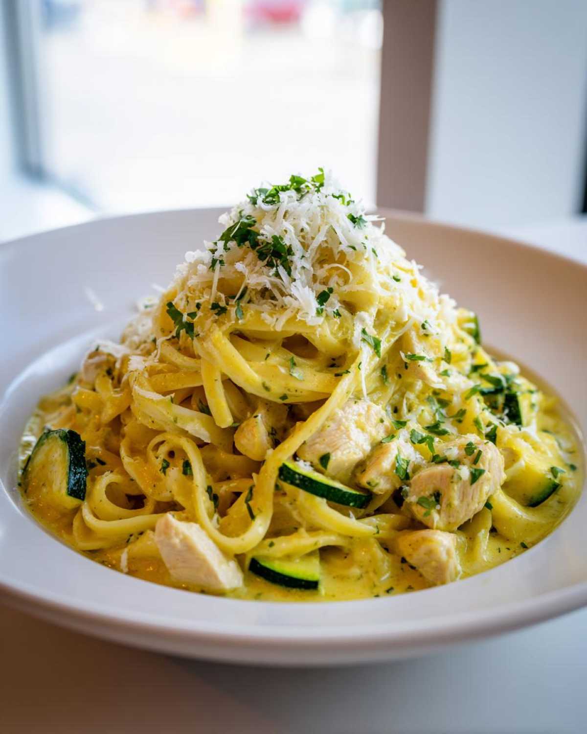A close-up of Lemon Chicken Pasta with Zucchini and Parmesan, topped with grated cheese and parsley.