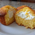 Close-up of a Lemon Muffins with Cream Cheese Filling cut in half, showing the bright yellow cake and white filling.