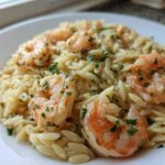 A close-up view of creamy Lemon Orzo Shrimp garnished with fresh parsley, served on a white plate.